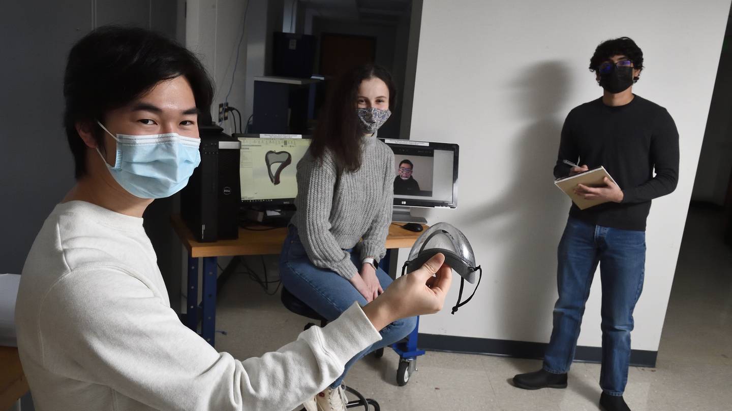 Three masked students in a lab space work with a mask prototype