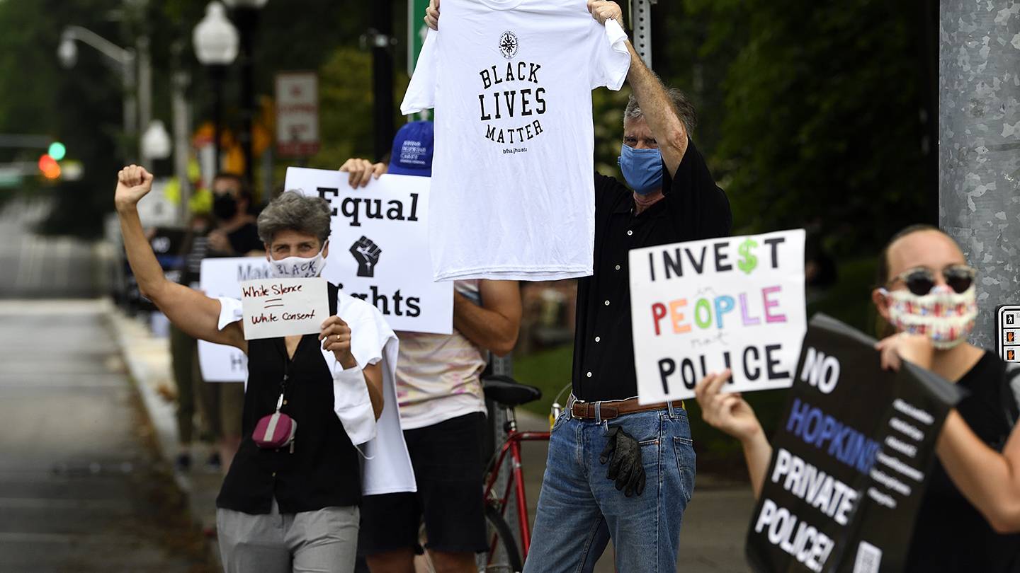 Protesters hold signs advocating for defunding the police and reading 'Black Lives Matter'
