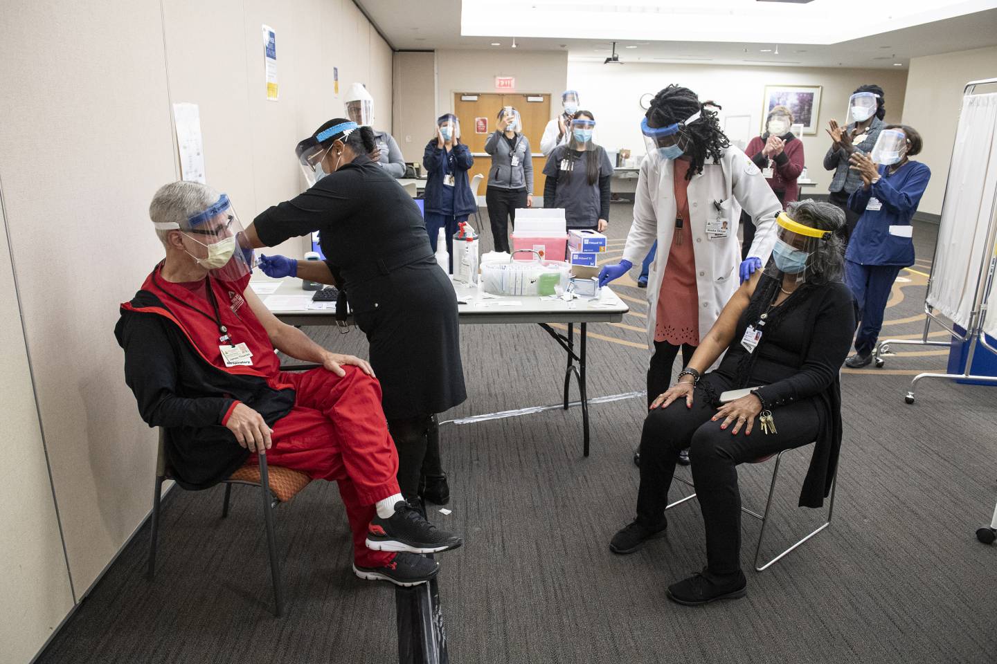 An audience of nurses applauds as the first two health care workers are vaccinated at Sibley Memorial Hospital