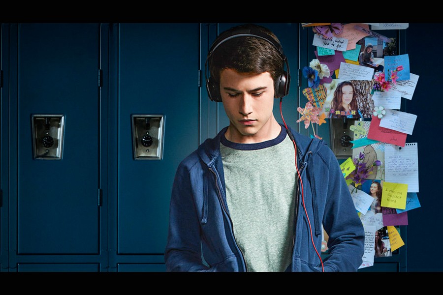 A young man wears headphones and stands in front of a line of lockers, one of which is decorated with messages and cards in a memorial