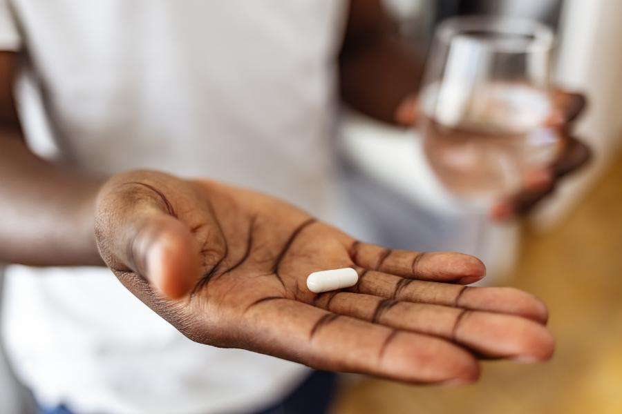 A person holds a white pill in the palm of their hand and a glass of water in the other