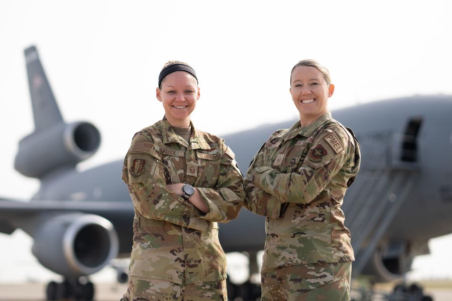 Two women in military uniforms pose in front of a military jet