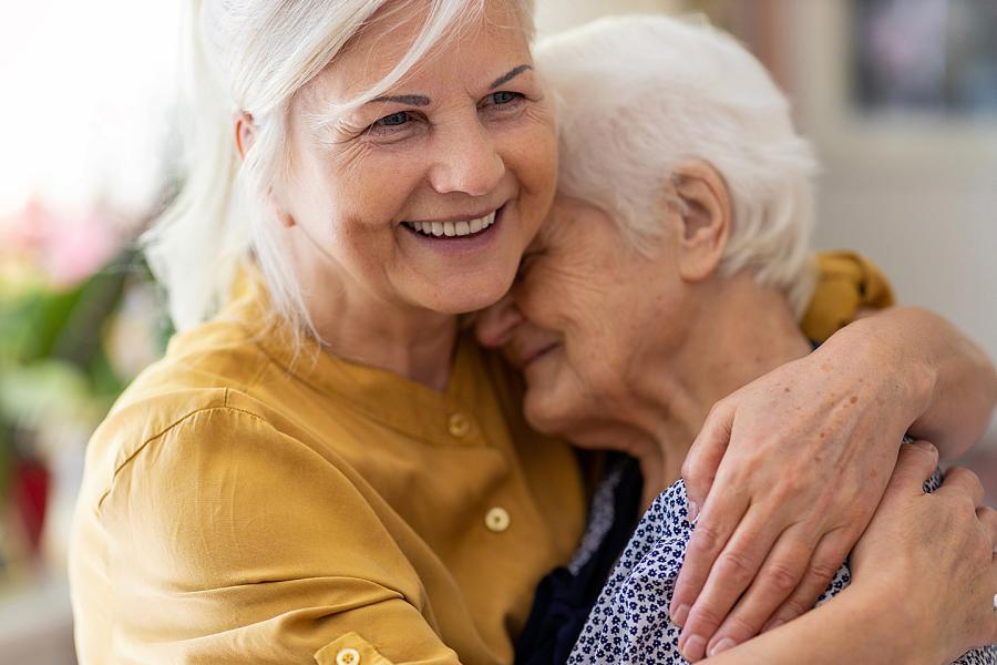 A middle-aged woman hugs her elderly mother