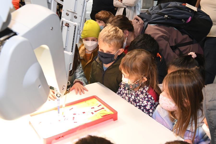 Children from the Early Learning Center gather around the da Vinci robot demonstration using the game Operation