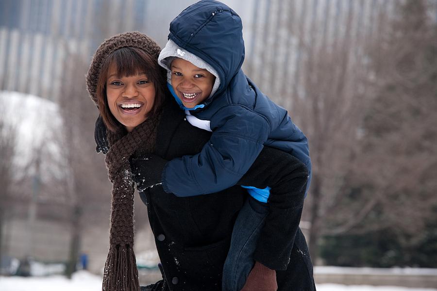 Laughing woman carries her young son piggyback in a snowy park