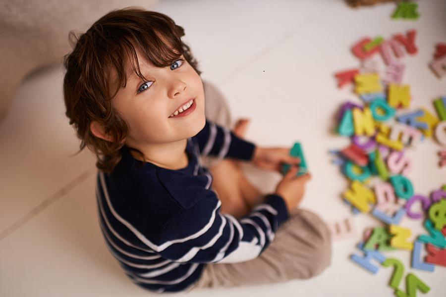 A young boy sits on the floor playing with colorful toy letters