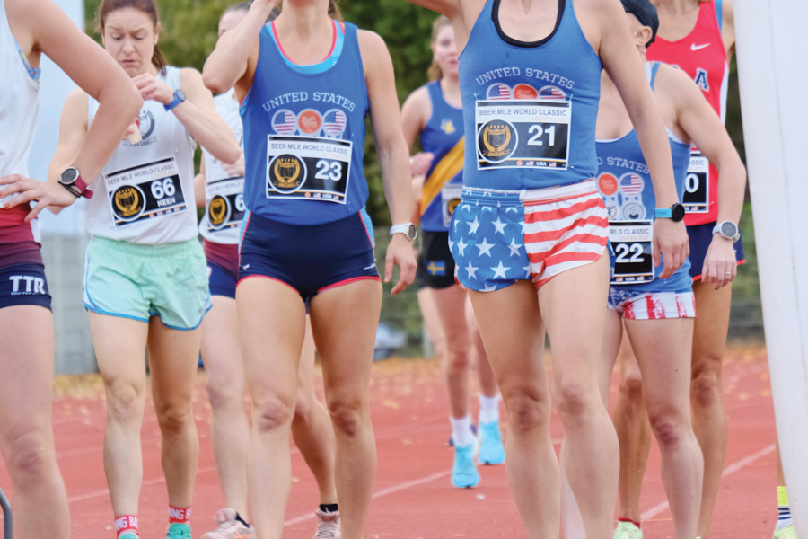 Elizabeth Laseter chugs a beer while standing among a group of runners on a track 