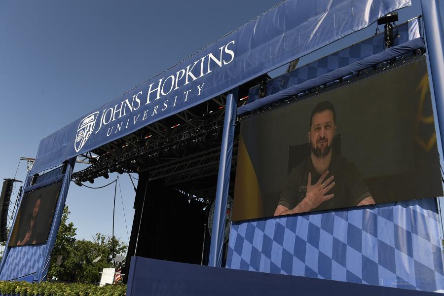 Volodymyr Zelenskyy, President of Ukraine, is seen on a large video screen under a banner reading 'Johns Hopkins University'