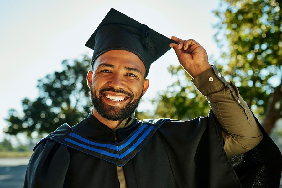 A mature man in an academic robe and mortarboard smiles after receiving his college degree