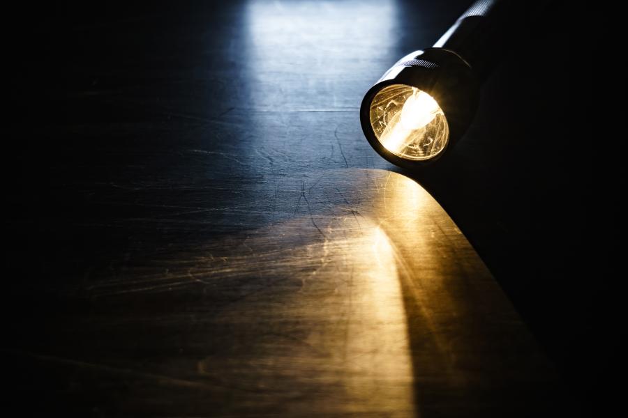 A lit-up flashlight lies on a wooden floor.