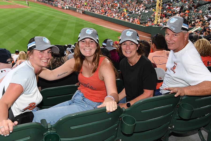 Three smiling women and a man in Johns Hopkins Orioles caps at Hopkins Night 2022 