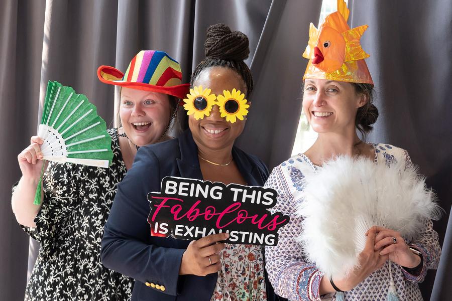 Three women from the Krieger School of Arts and Sciences pose for a photographer wearing party items such as funny hats and sunglasses.