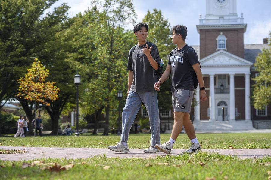 Two students chat while walking in front of Gilman Hall