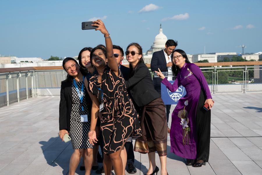 A group of six women gathers for a selfie on the roof of a building; the U.S. Capitol dome is visible in the background