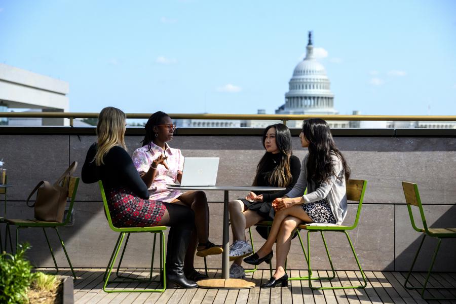 People at a rooftop table at Johns Hopkins University Bloomberg Center at 555 Pennsylvania Ave. with the Capitol in the background