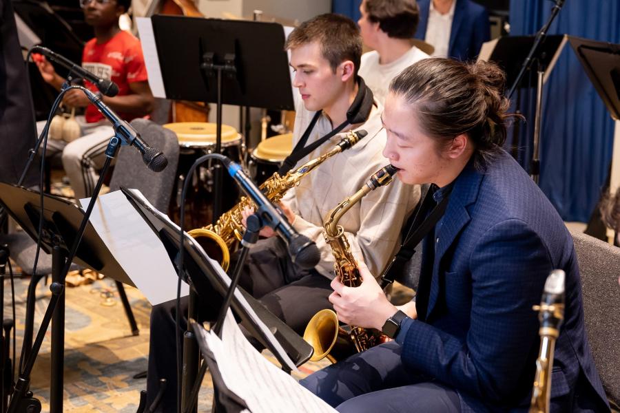 Two saxophonists visible in center with parts of other instruments and musicians seen surrounding them