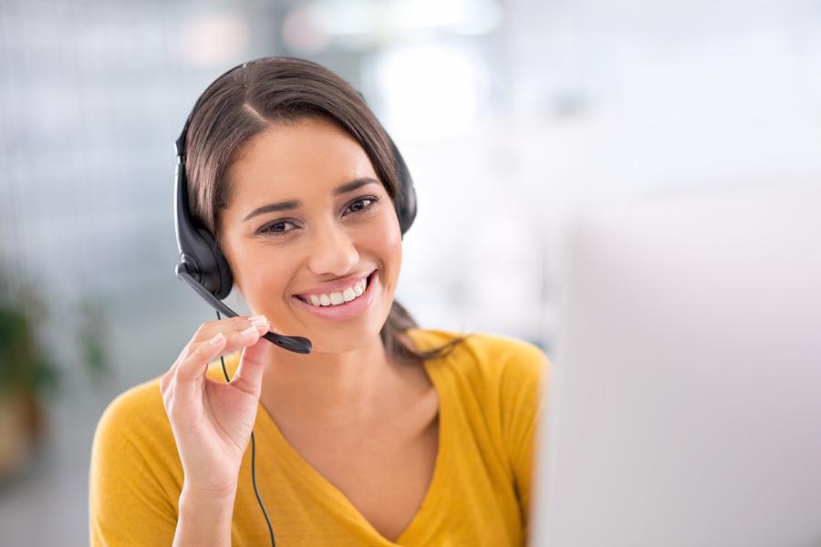 A smiling customer representative wearing a phone headset talks with a client.