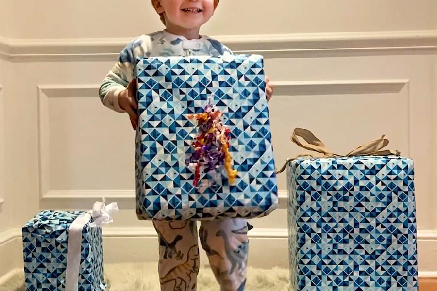 A cute kiddo in holiday pajamas shakes wrapped presents to try to figure out what's inside