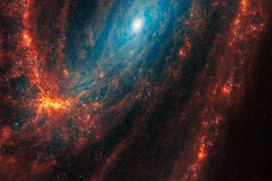 Spiral galaxy NGC 3627: the gas and dust stand out in stark shades of orange and red, and show finer spiral shapes with the appearance of jagged edges, though these areas are still diffuse