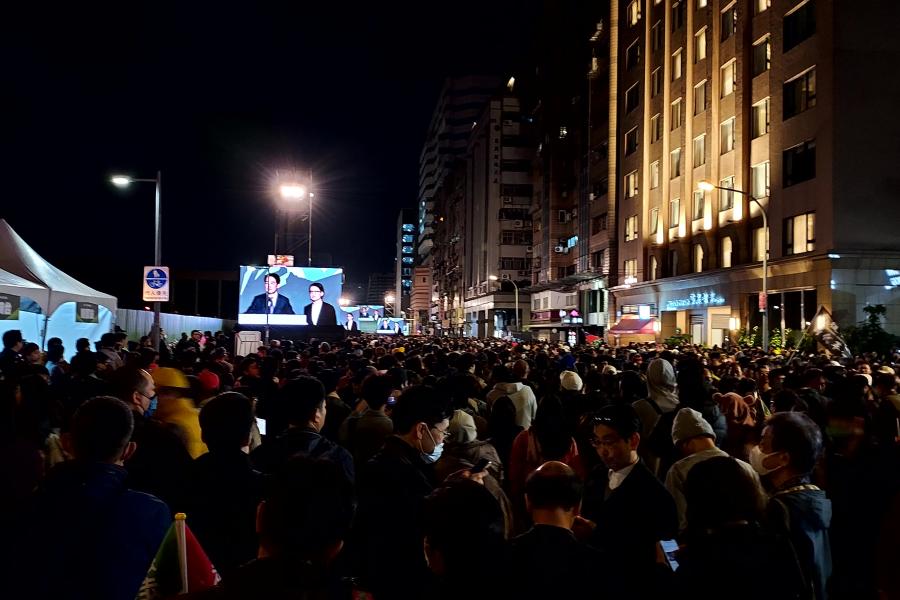 A large crowd gathers outdoors at night to view Taiwan election winners on a giant video screen
