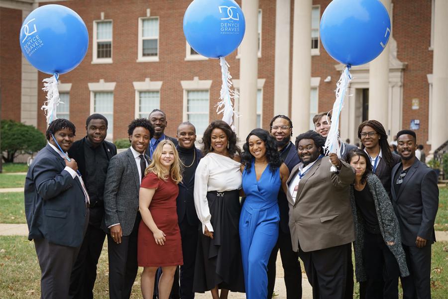 A group of 13 students from the Denyce Graves Foundation stand around Denyce holding large blue balloons
