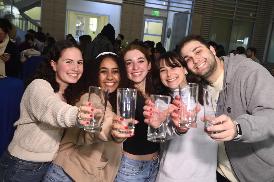 Five students hold out empty glasses while smiling for the camera