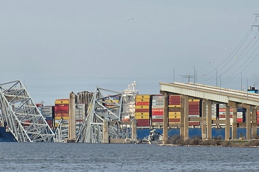 Pieces of a collapsed bridge in the water next to large container ship