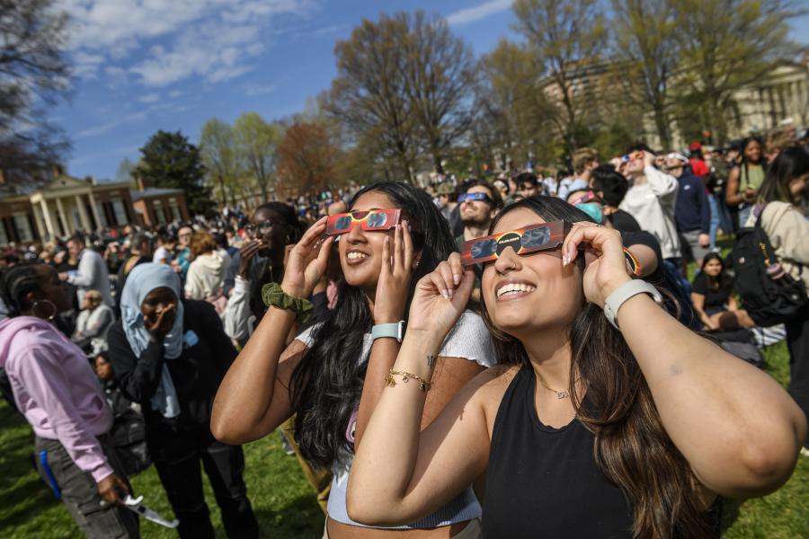 Two college students look up at the sky while wearing solar eclipse glasses.
