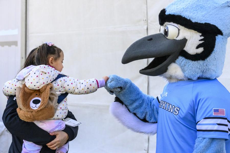 A little girl wearing a teddy bear backpack gives Jay a fist bump