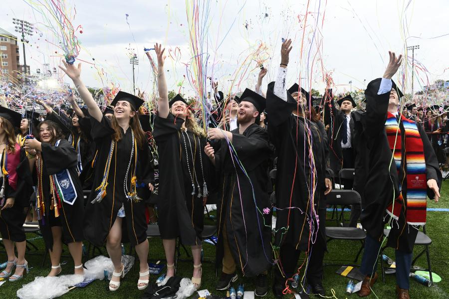 A crowd of graduating students shoot colorful streamers up into the air.