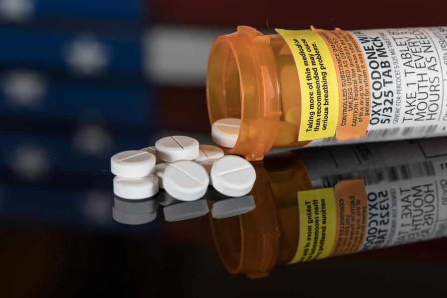 Prescription bottle for Oxycodone tablets and pills on wooden table with USA flag in background