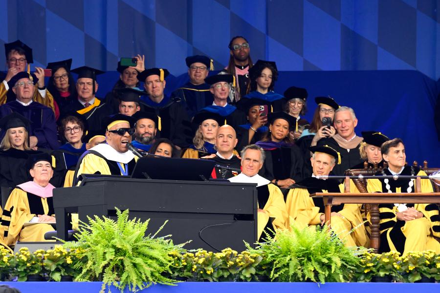 Stevie Wonder performs at the piano as dozens of university leaders in graduation regalia look on