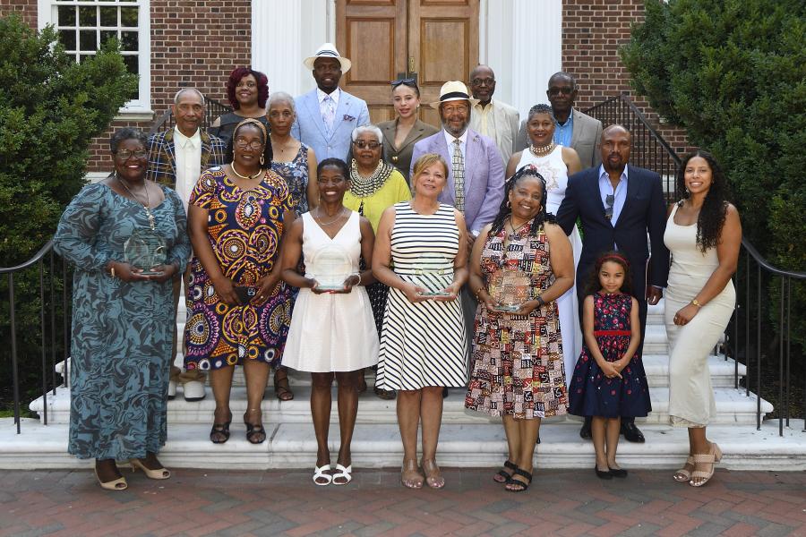 A group of people pose for a photo on an outdoor marble staircase. Several of them are holding awards made of glass.