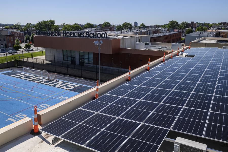 Solar panels cover the roof of the Henderson-Hopkins School. Below the roof is a sky-blue sports field.