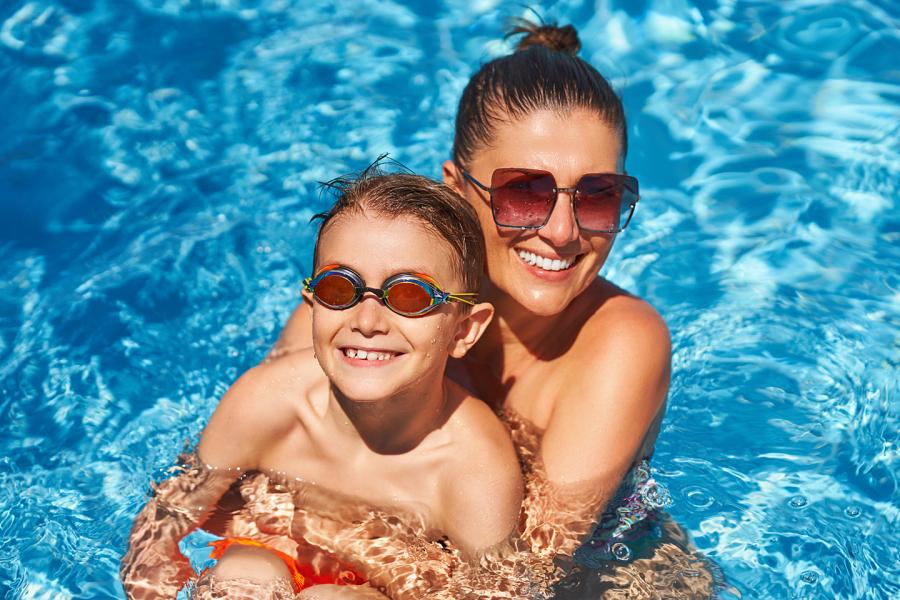 Smiling woman hugs her young sun in a swimming pool