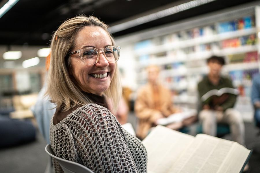A middle-aged woman holds a book in a university library