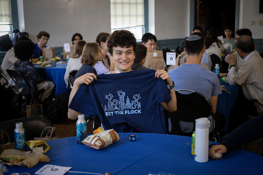 A student smiles while holding up a blue t-shirt that says 