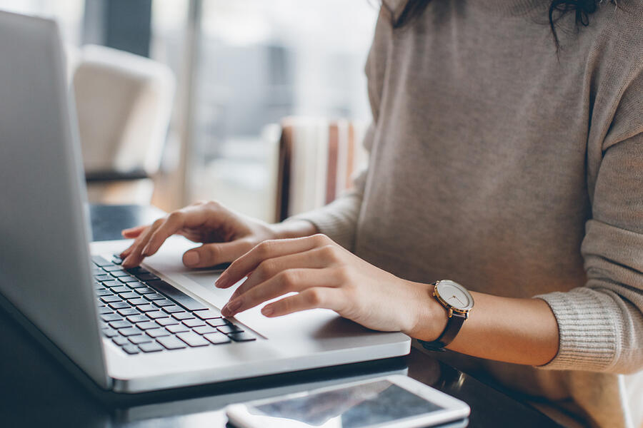 A closeup of a young woman's hands working on a laptop