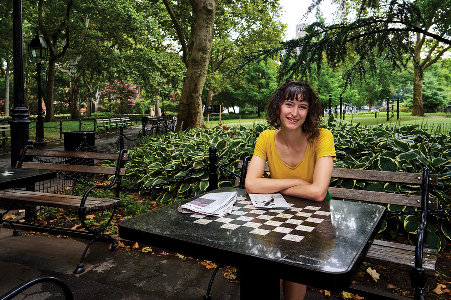 Zoe Bell, a white woman with short brown hair, sits in a park at a table that's painted to look like a checkerboard