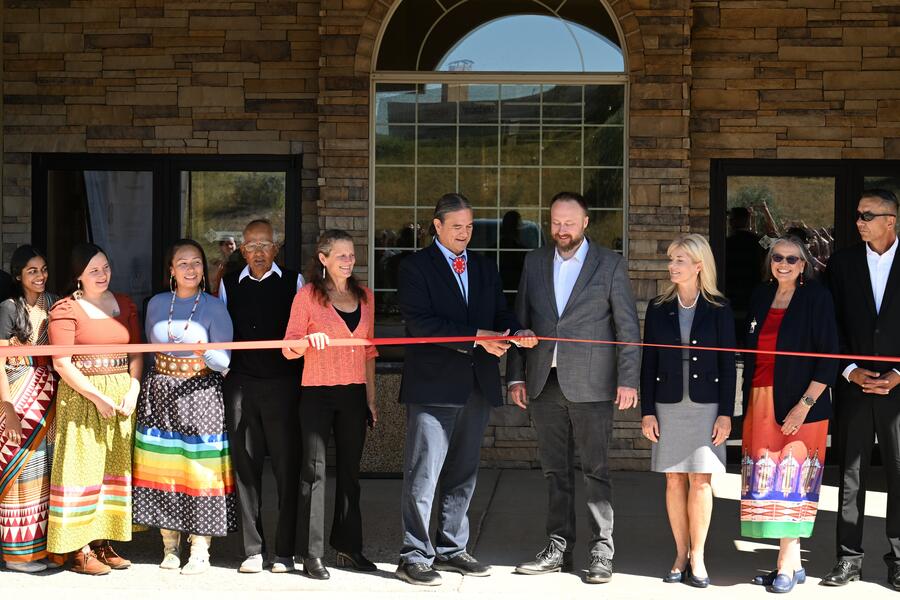 A group of people stand in front of the new Great Plains Hub building as David Warne cuts a ribbon that stretches across the building