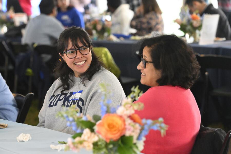 Two people chat while sitting at a banquet table. Another table full of people sits behind them.