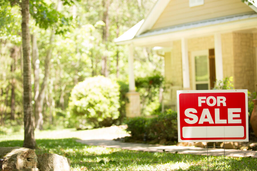 A modest yellow house with a for sale sign in the front yard