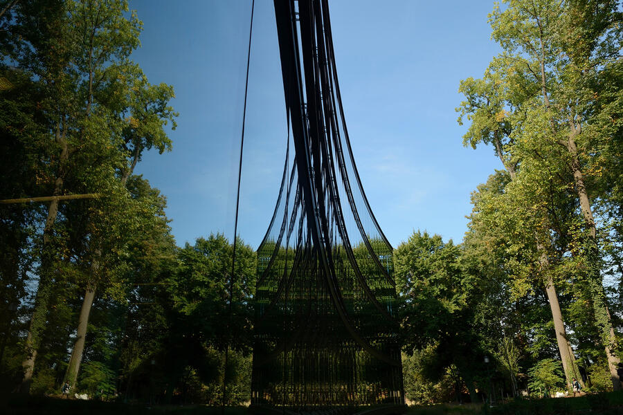 Tall, green trees are seen on the left of this photo and also reflected in the curve, mirrored glass facade of a campus building on the left