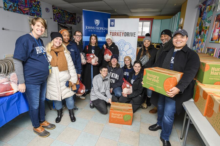 A group of volunteers smile for the camera at the Vernon Rice Memorial Turkey drive. Some are holding frozen turkeys or boxes of food.