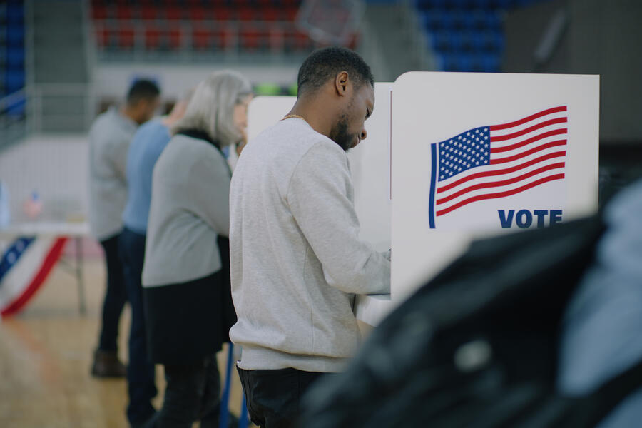 People voting in rows of voting booths with American flags on the side.