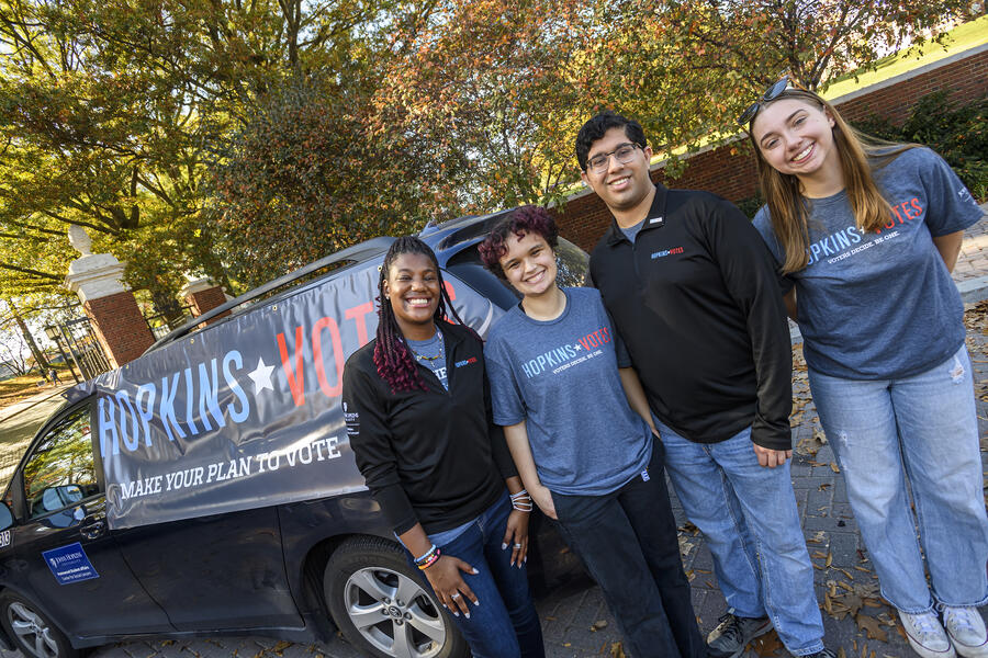 Students stand in front of a Hopkins Votes banner on a shuttle van