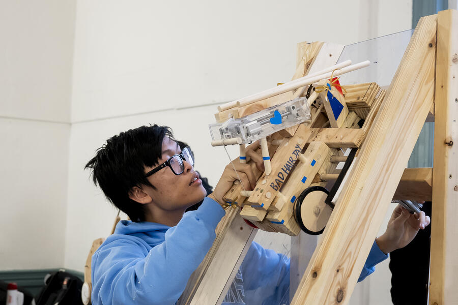 A male student sets up a wooden vehicle on a wooden ramp