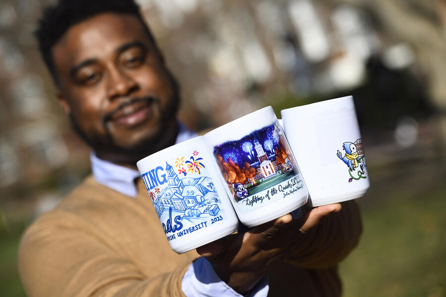 An adult holds up three Lighting of the Quads souvenir mugs from different years.