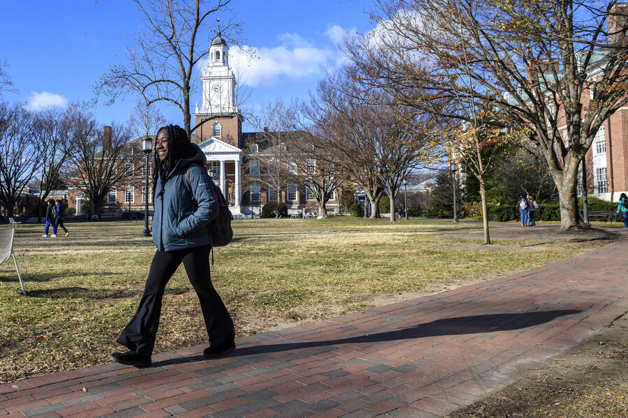 A student smiles while walking on brick pathway with Gilman Hall in the background