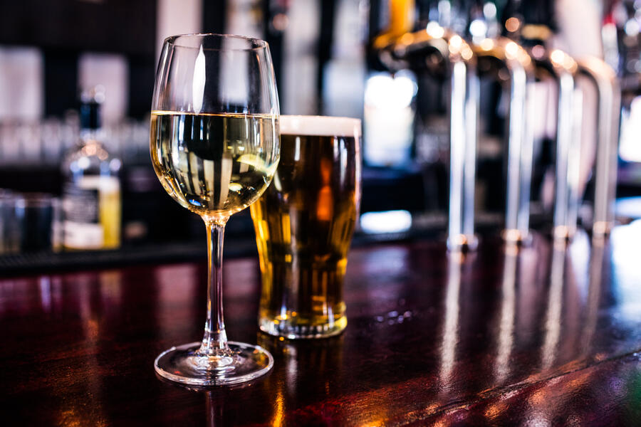 A glass of wine and a pint of beer sit on a wooden bar